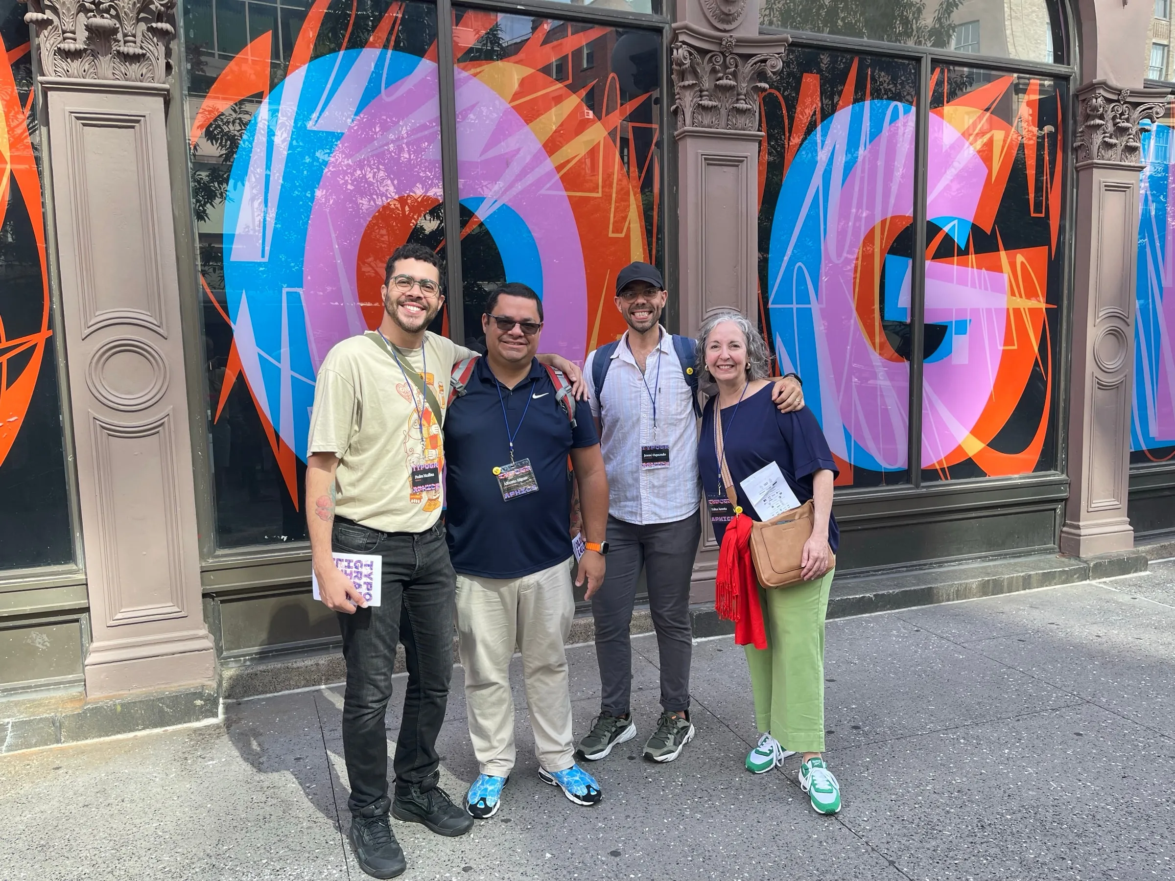 Pedro with Josué, Alberto and Edna, wearing Typographics badges, in front of a storefront painted with large letterforms