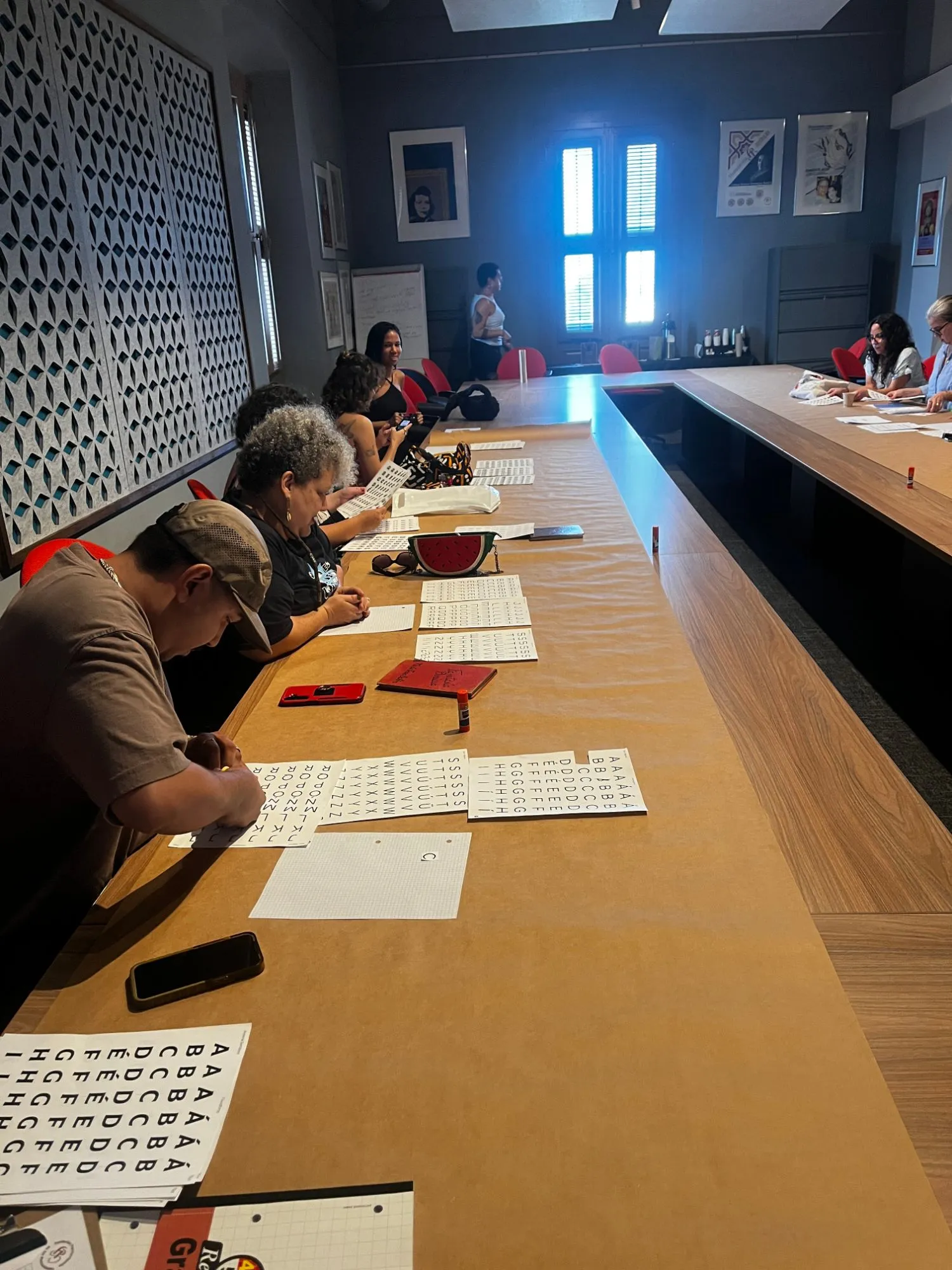 Workshop participants along a long table, cutting and arranging printed sheets of letters